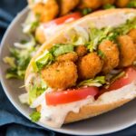 A hoagie roll filled with fried shrimp, dressing, tomato, and lettuce on a plate