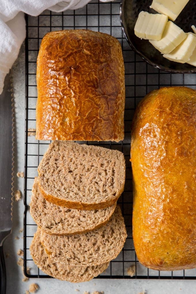 two loaves of whole wheat bread on a cooling rack. One loaf sliced into a few pieces.