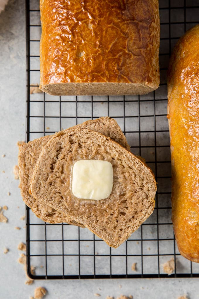 two slices of whole wheat bread on a cooling rack with a slice of butter on top