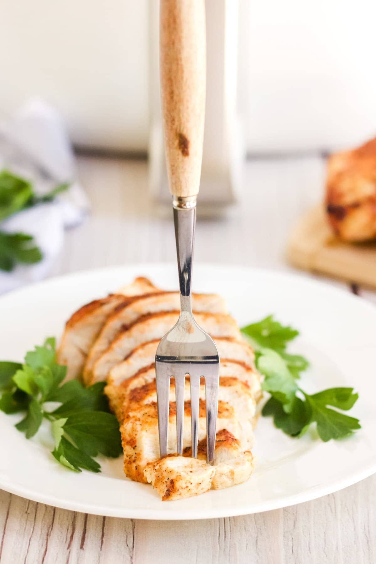 sliced chicken breast on a whilte plate with parsley and a fork