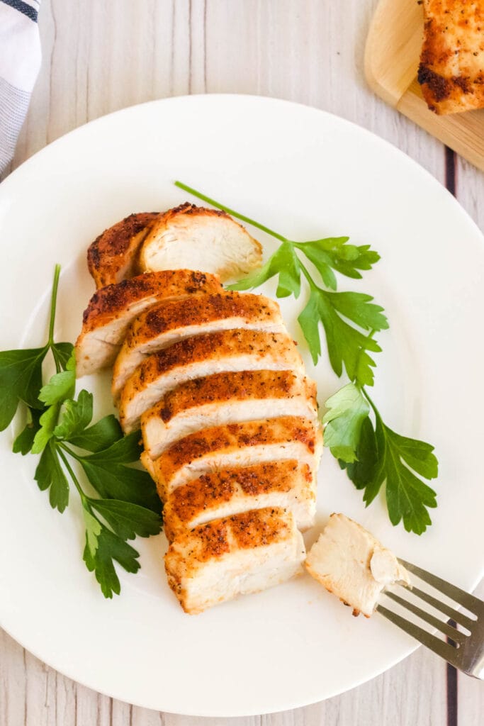sliced chicken breast with parsley o a white plate and white wood background