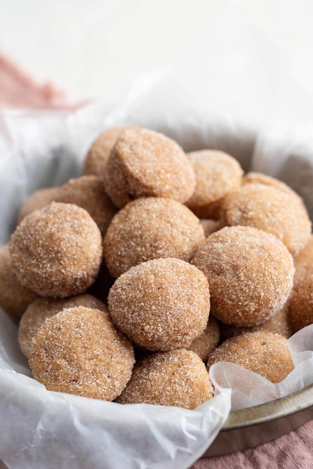 donut holes in a basket with a white towel, coated in cinnamon sugar