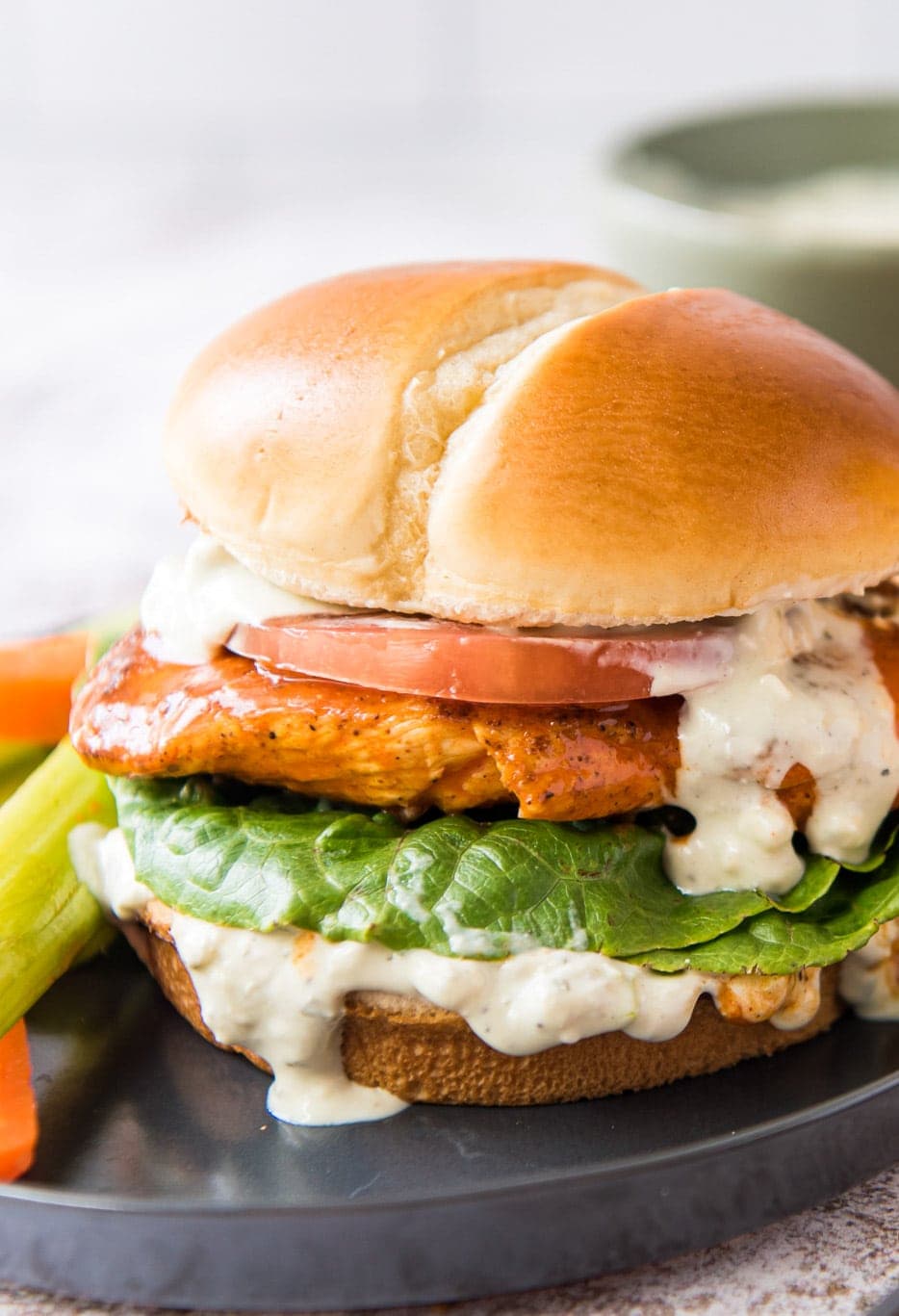 a black plate with a buffalo chicken sandwich on a brioche bun, celery, carrot sticks