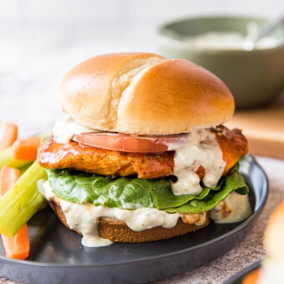 A sandwich with buffalo chicken and dressing sitting on a grey plate.