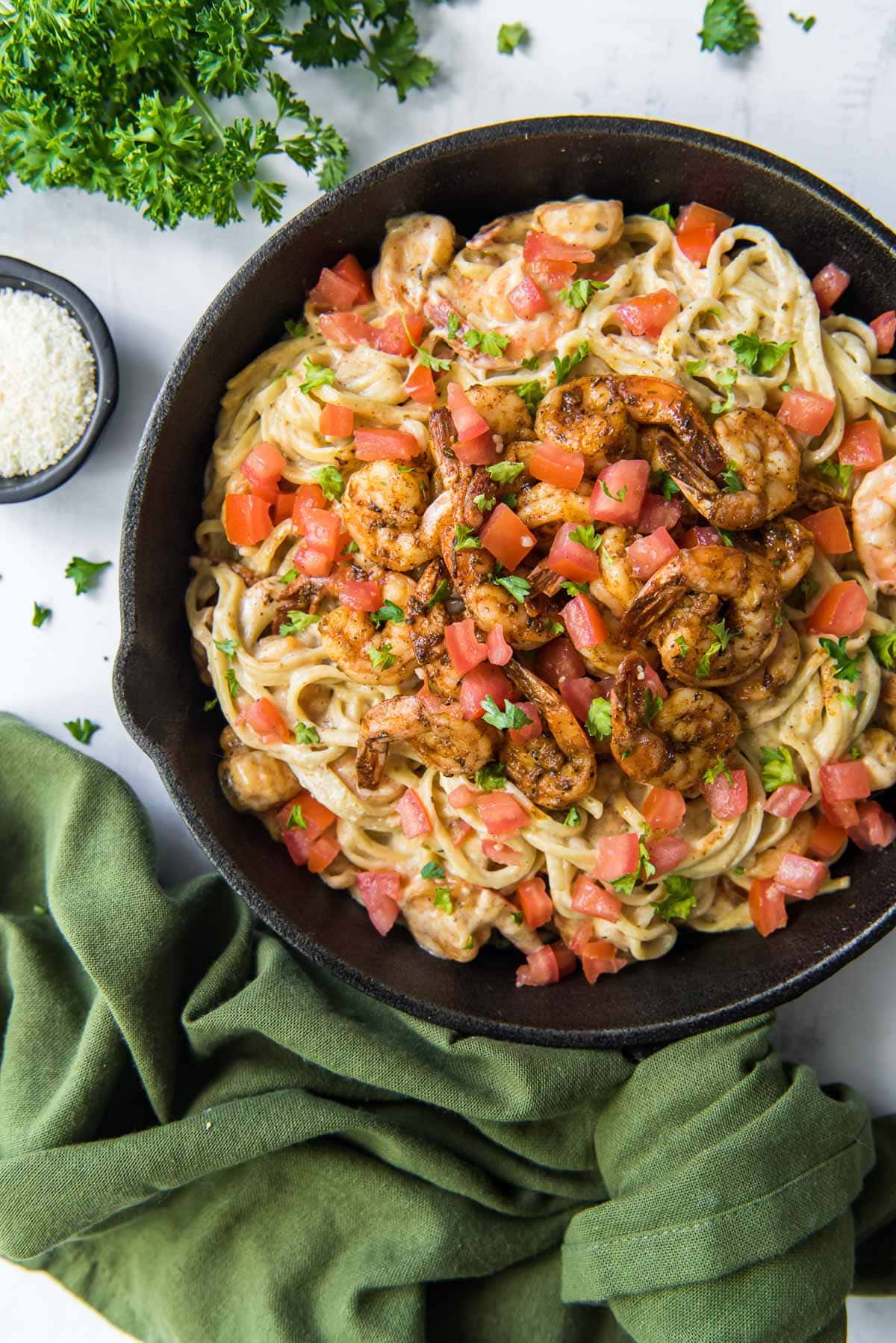 cast iron skillet with pasta and shrimp, tomatoes, green napkin