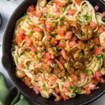 Cast iron pan full of creamy pasta, tomatoes, and cooked cajun shrimp.