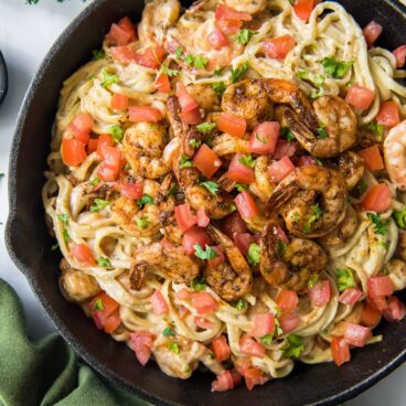 Cast iron pan full of creamy pasta, tomatoes, and cooked cajun shrimp.