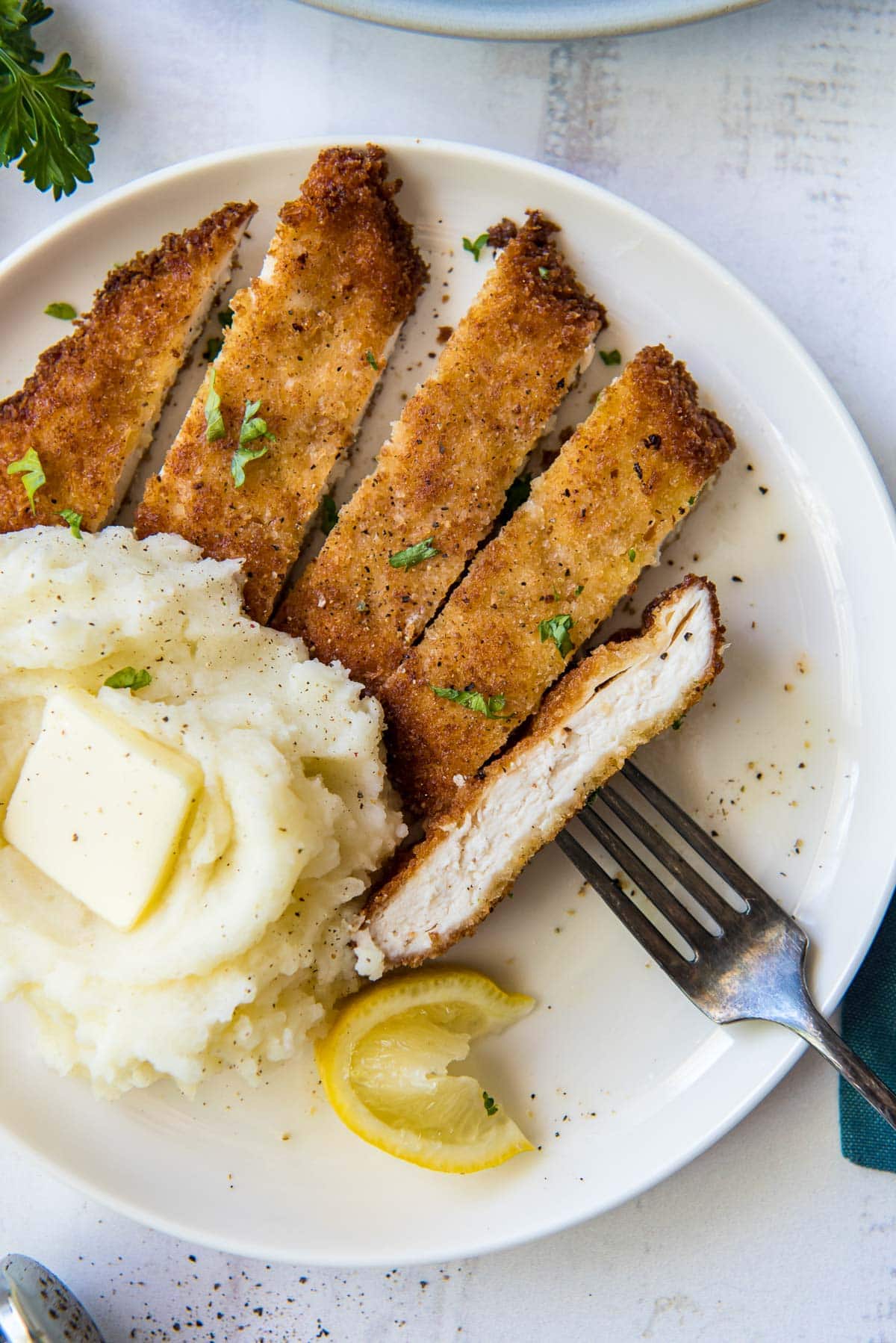 mashed potatoes and sliced breaded chicken on a white plate with a fork