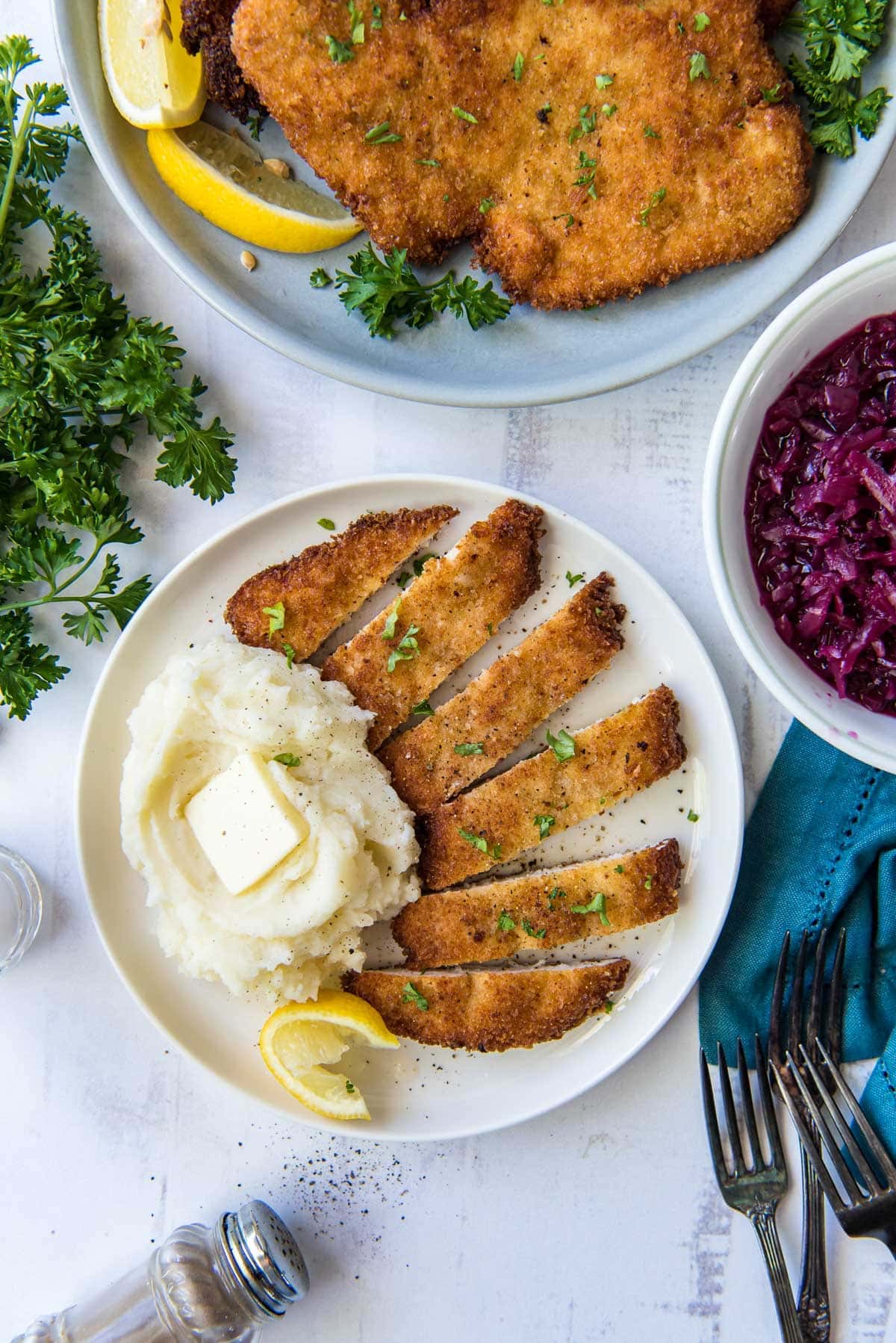 3 white plates, red cabbage, mashed potatoes, fried chicken cutlets, blue napkin, forks, parelsy