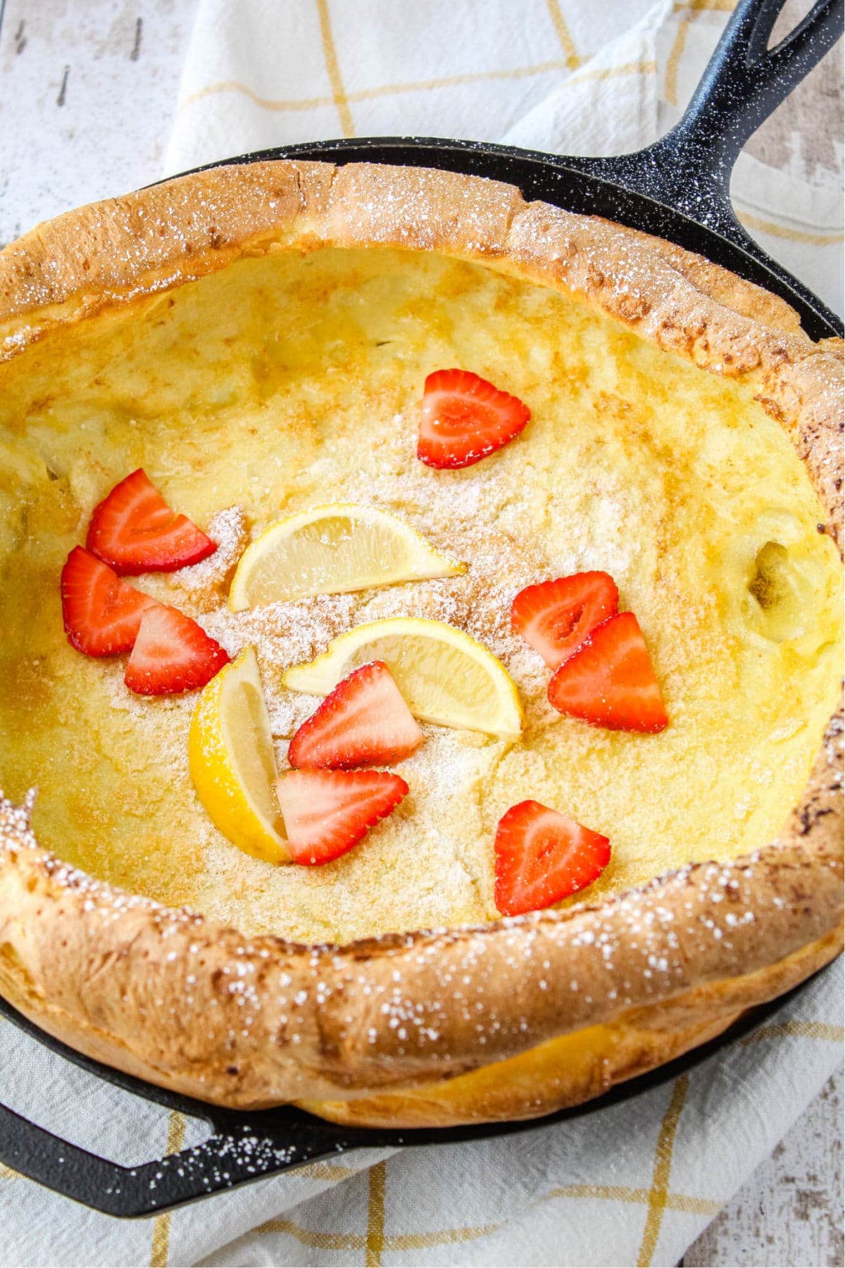 german pancake in a cast iron skillet after cooking, topped with powdered sugar, strawberries, and lemon