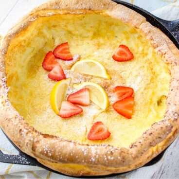 square image of german pancake topped with powdered sugar lemons and strawberries