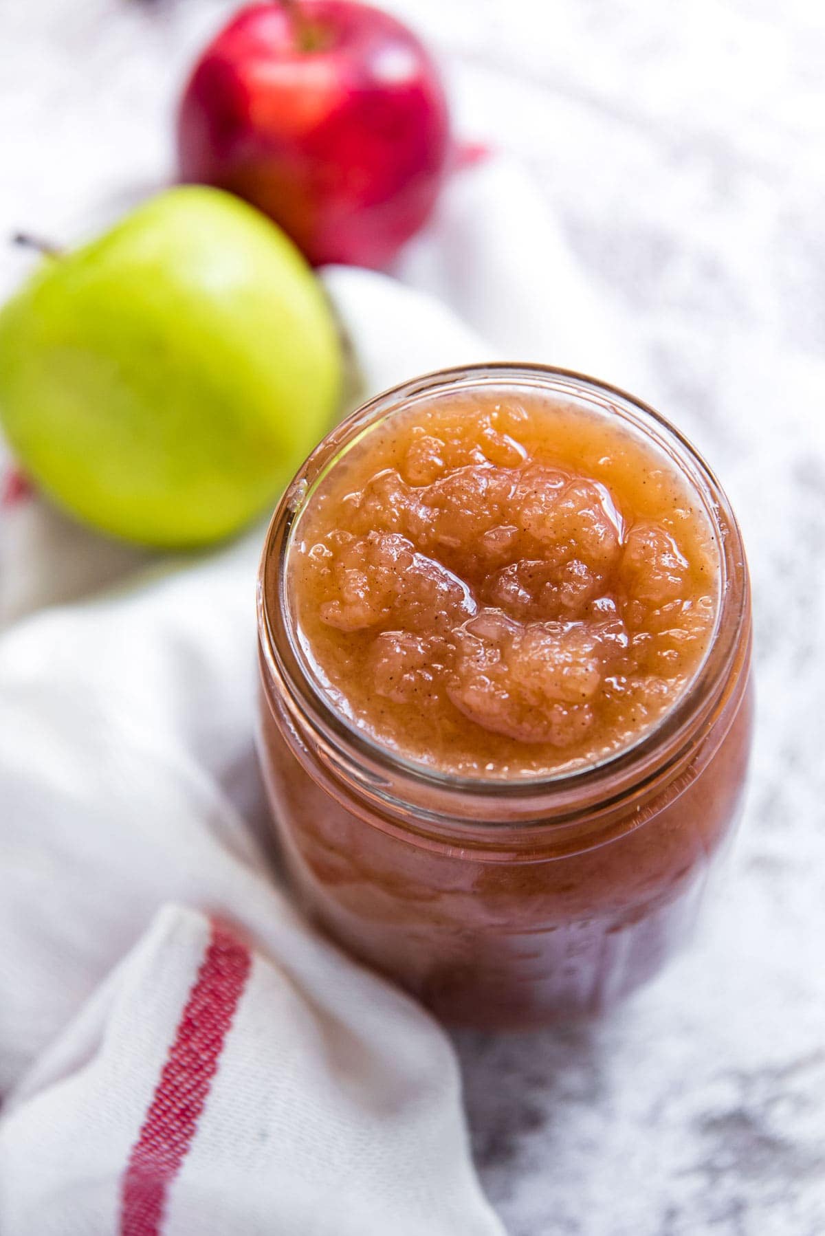 jar of homemade applesauce, white napkins with a red stripe, red apple, green apple
