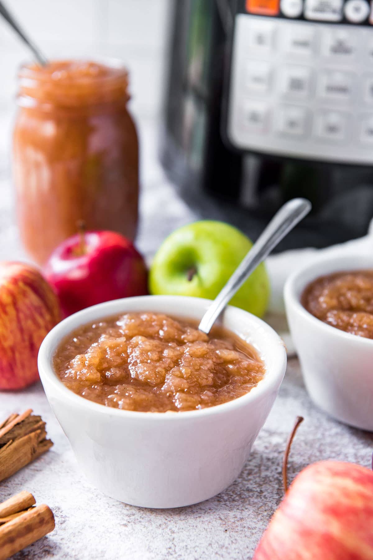 white dish of applesauce with spoon, apples, instant pot, cinnamon sticks