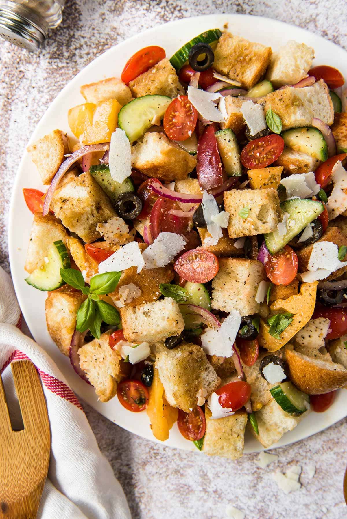 white plate, chunks of bread, olives, tomatoes, cucumber and parmesan cheese, wooden spoon