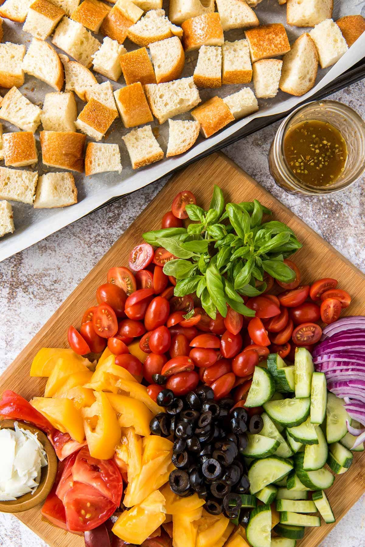 wood cutting board with tomatoes, peppers, olives, cucumbers, basil and bread