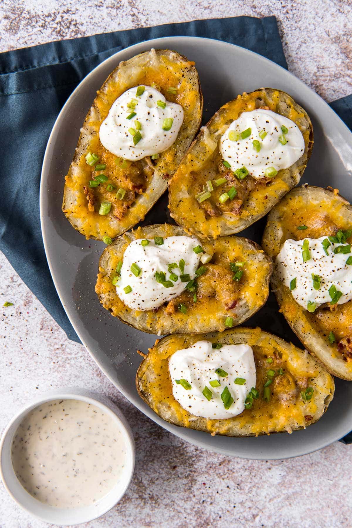 a white plate, blue napkin, dish of ranch, potato skins with cheese bacon chives and sour cream
