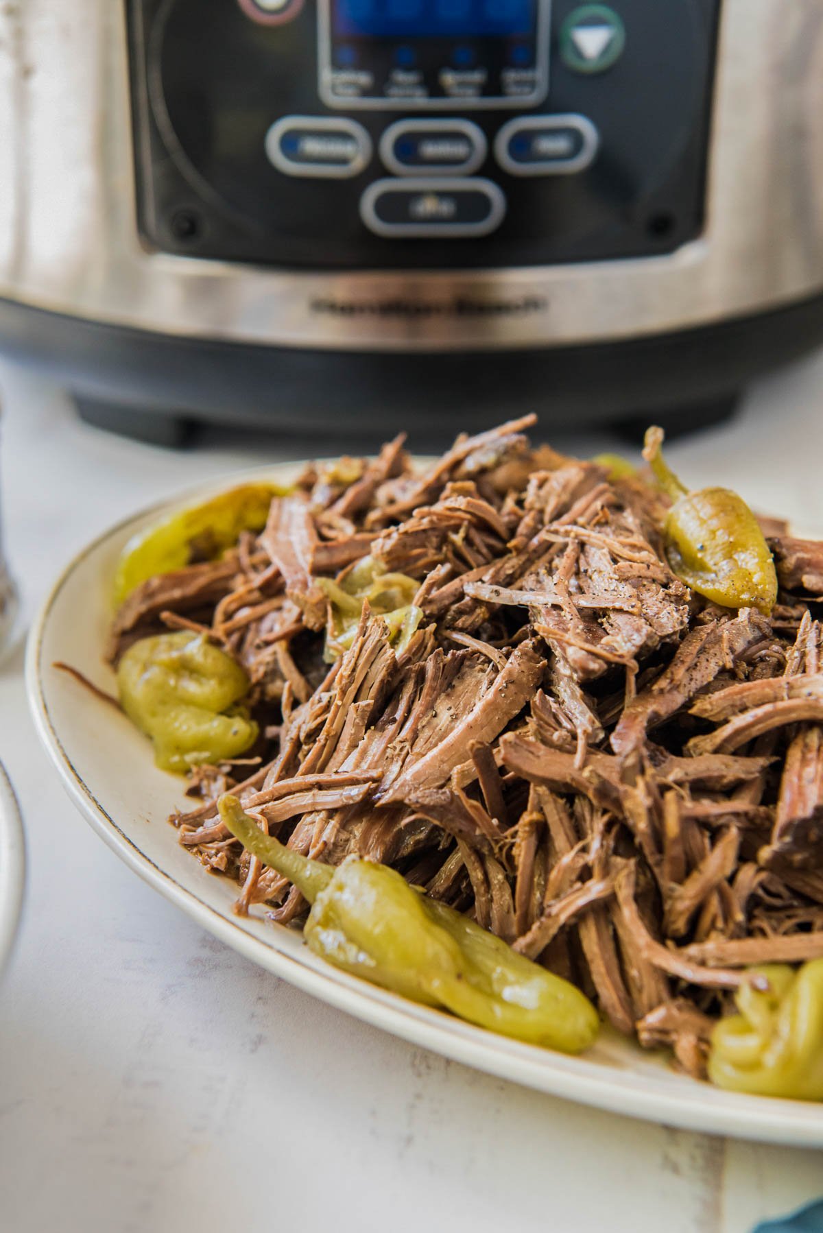 white platter with shredded beef and pepperoncinis, a slow cooker