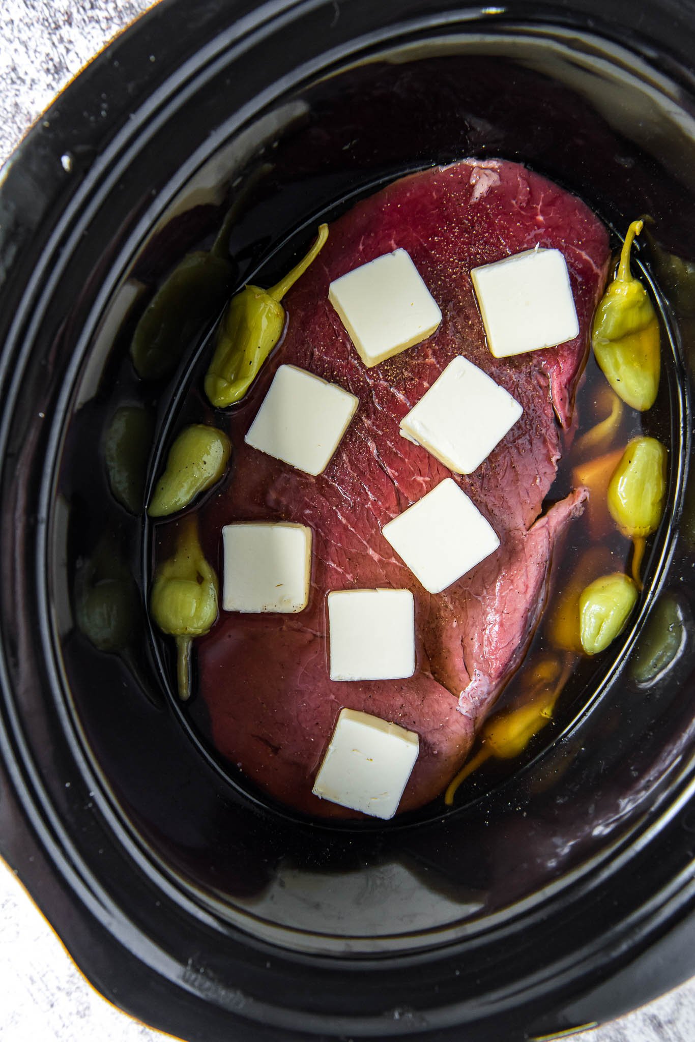 slow cooker with beef roast, slices of butter, pepperoncinis