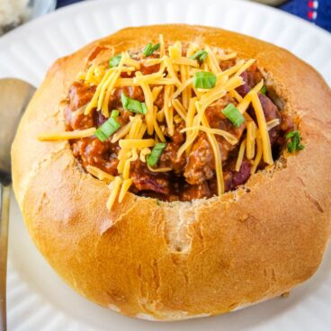 Bread bowl full of chili with a sprinkle of cheese and green onions.