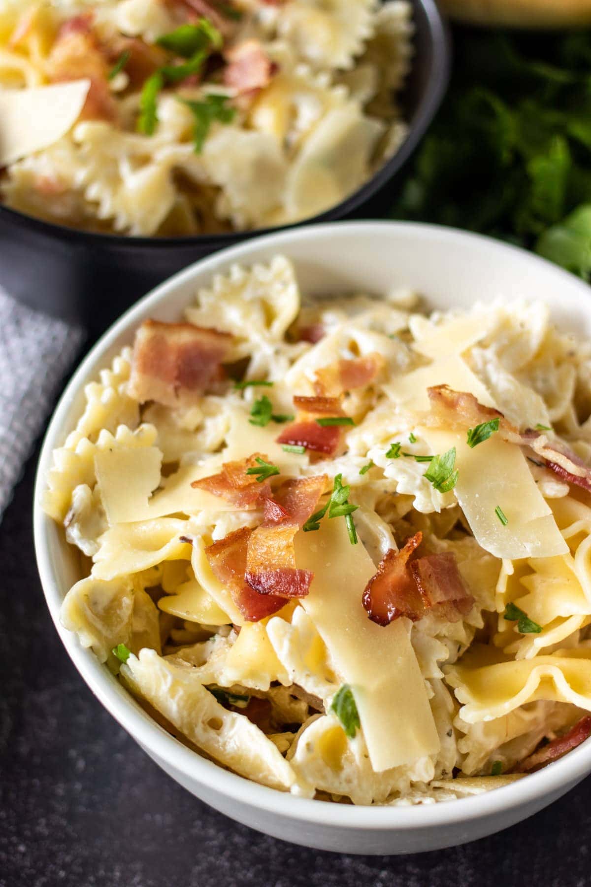 white bowl of pasta topped with bacon & parsley