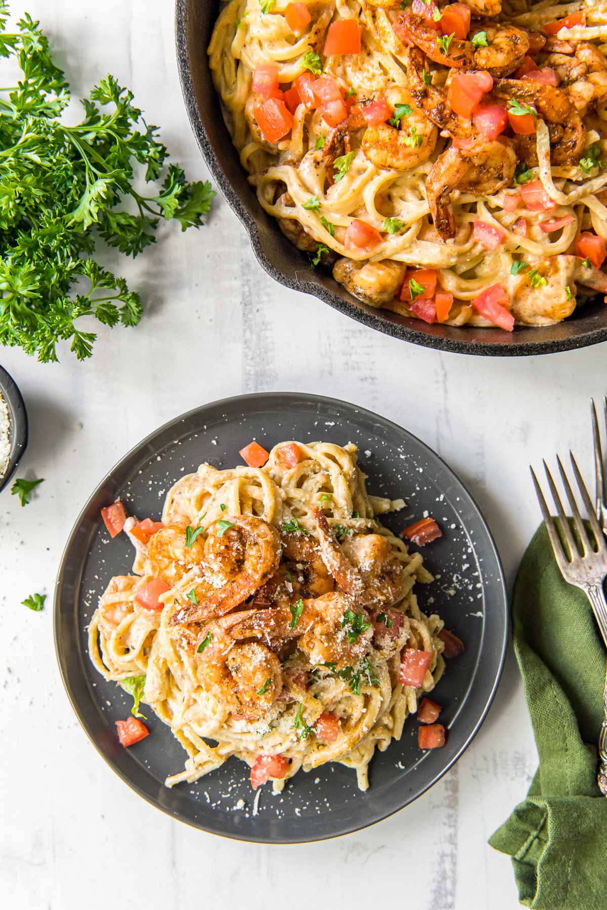 gray plate with pasta and cajun shrimp, cast iron skillet, parsley, green napkin, fork