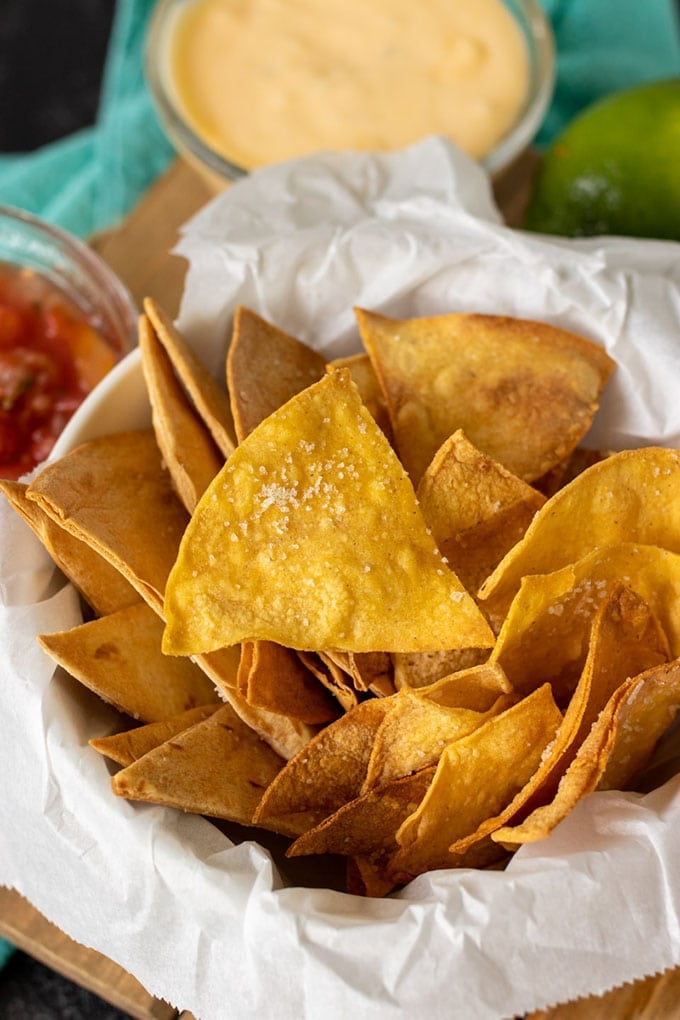 basket of homemade tortilla chips, dish of salsa, dish of cheese sace, limes, blue towel