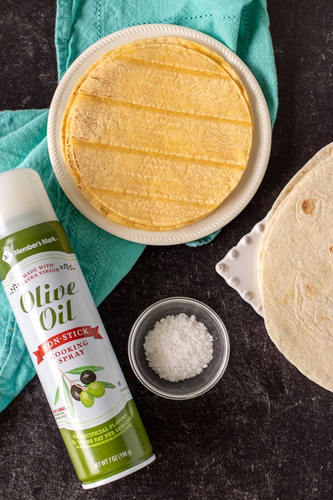 overhead shot of tortillas, olive oil spray, and salt with a blue napkin