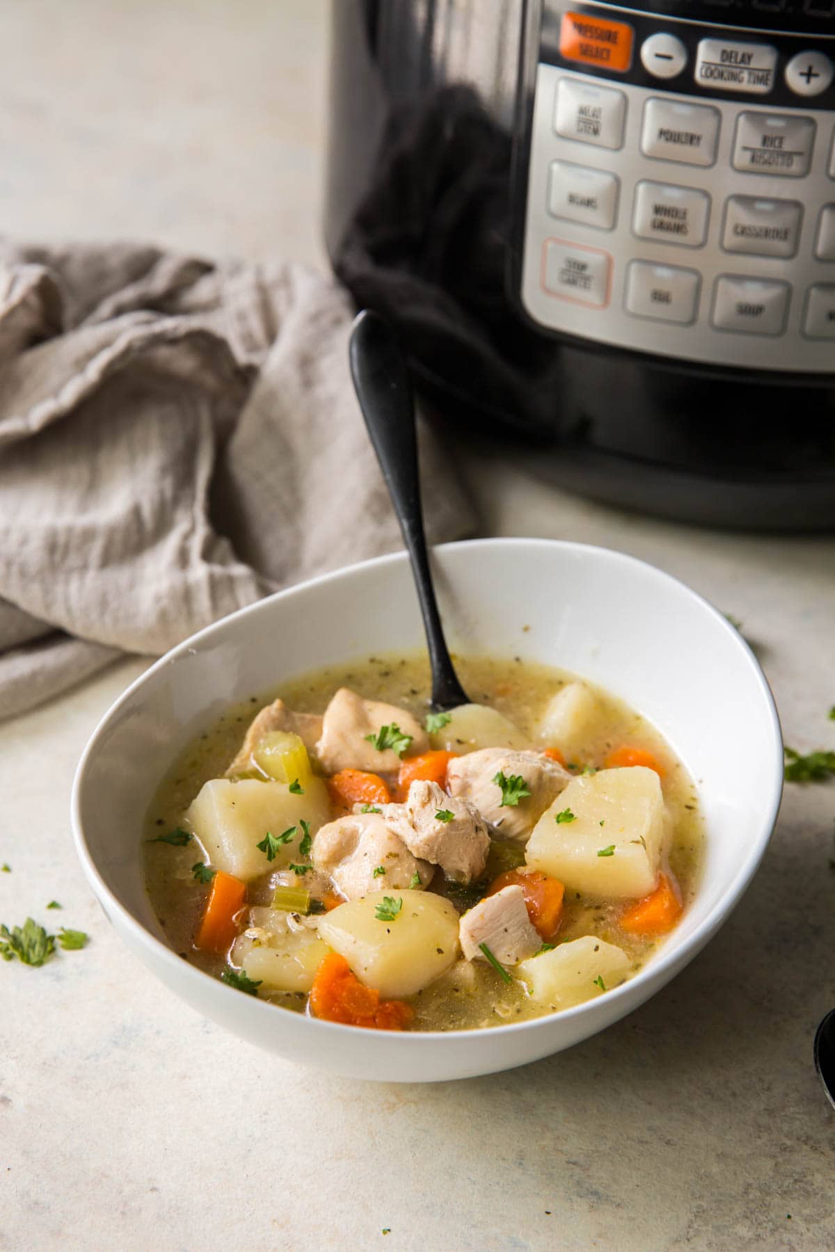 chicken stew in a white bowl on a table next to an instant pot