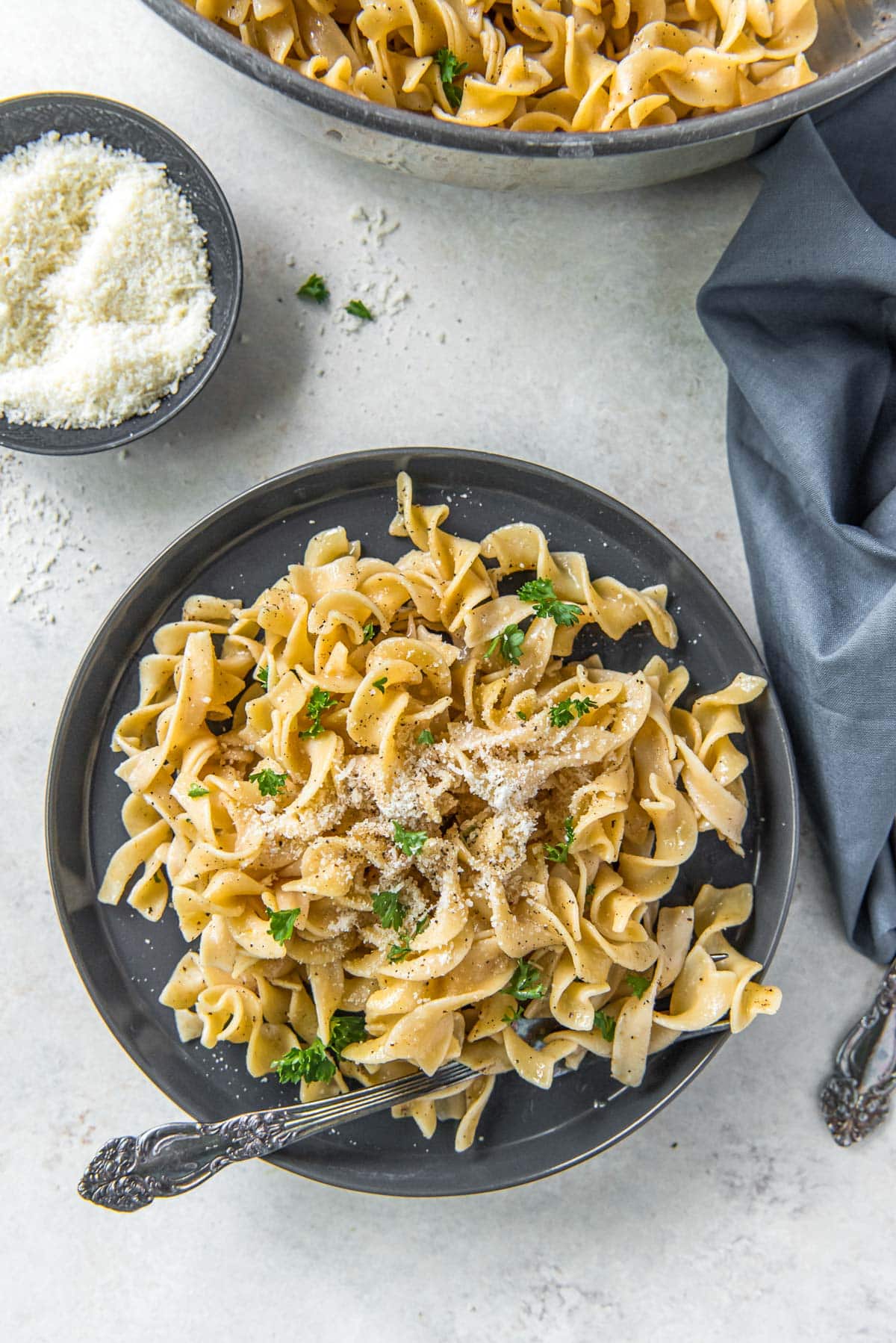 gray plate, egg noodles with parmesan cheese, gray napkin, forks