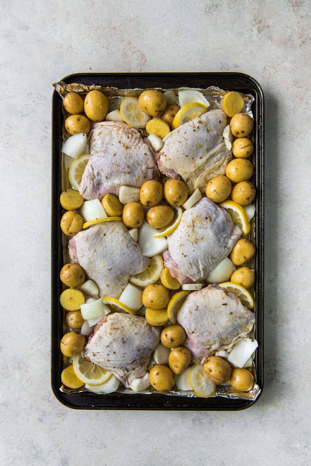 raw chicken thighs with skin, potatoes, onions and lemon slices