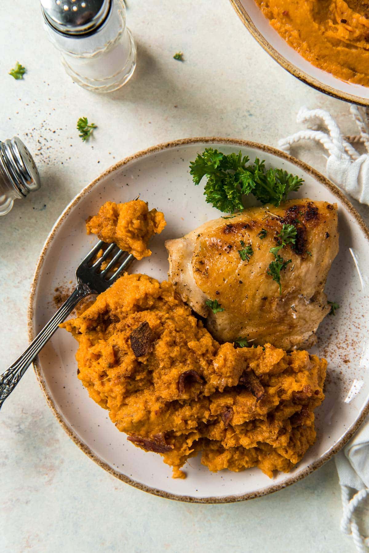 white plate, fork, mashed sweet potatoes, chicken thigh, salt shaker