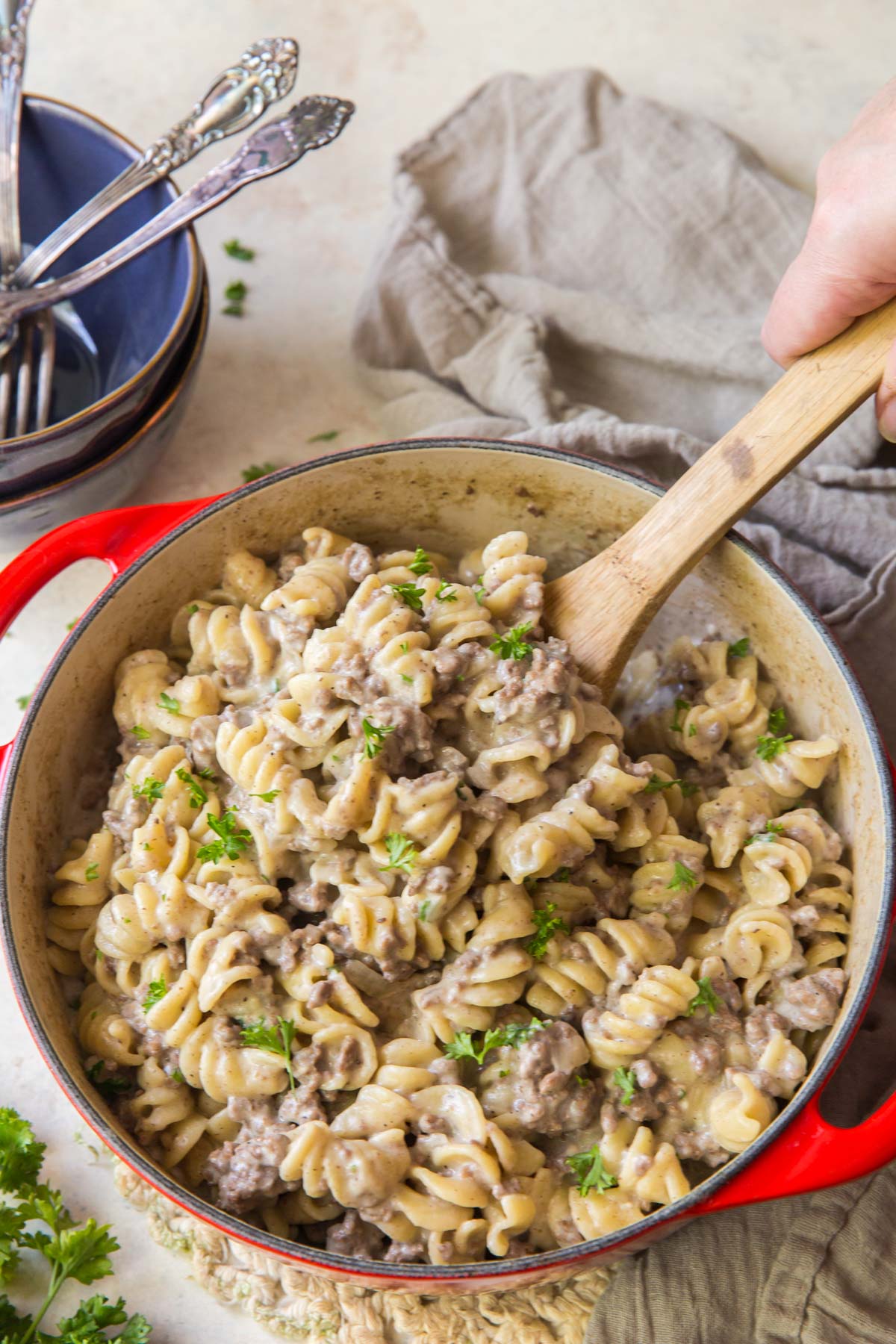 noodles, ground beef, creamy sauce, wood spoon, blue bowls, forks, gray napkin