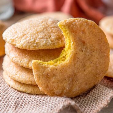 pumpkin sugar cookies, stacked, one has a bite out of it, orange napkin, burlap