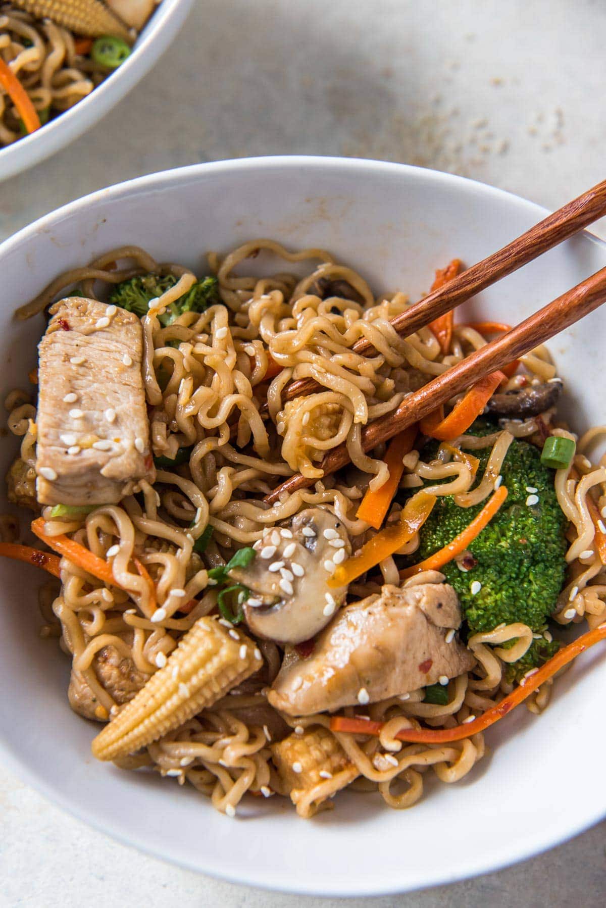 ramen noodles, chicken and vegetables in a white bowl with chopsticks