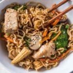 ramen noodles, chicken and vegetables in a white bowl with chopsticks