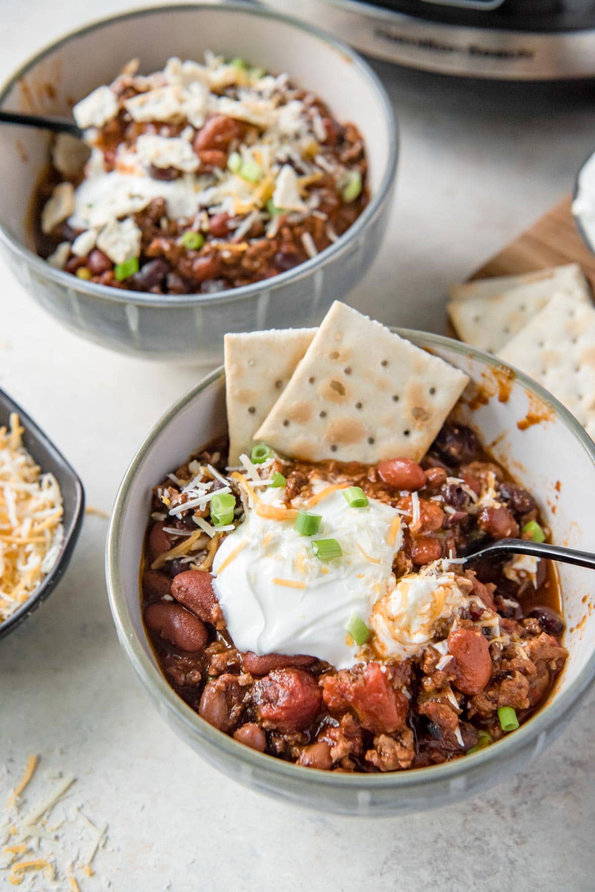 bowls with chili, sour cream, cheese, and crackers, spoon, slow cooker