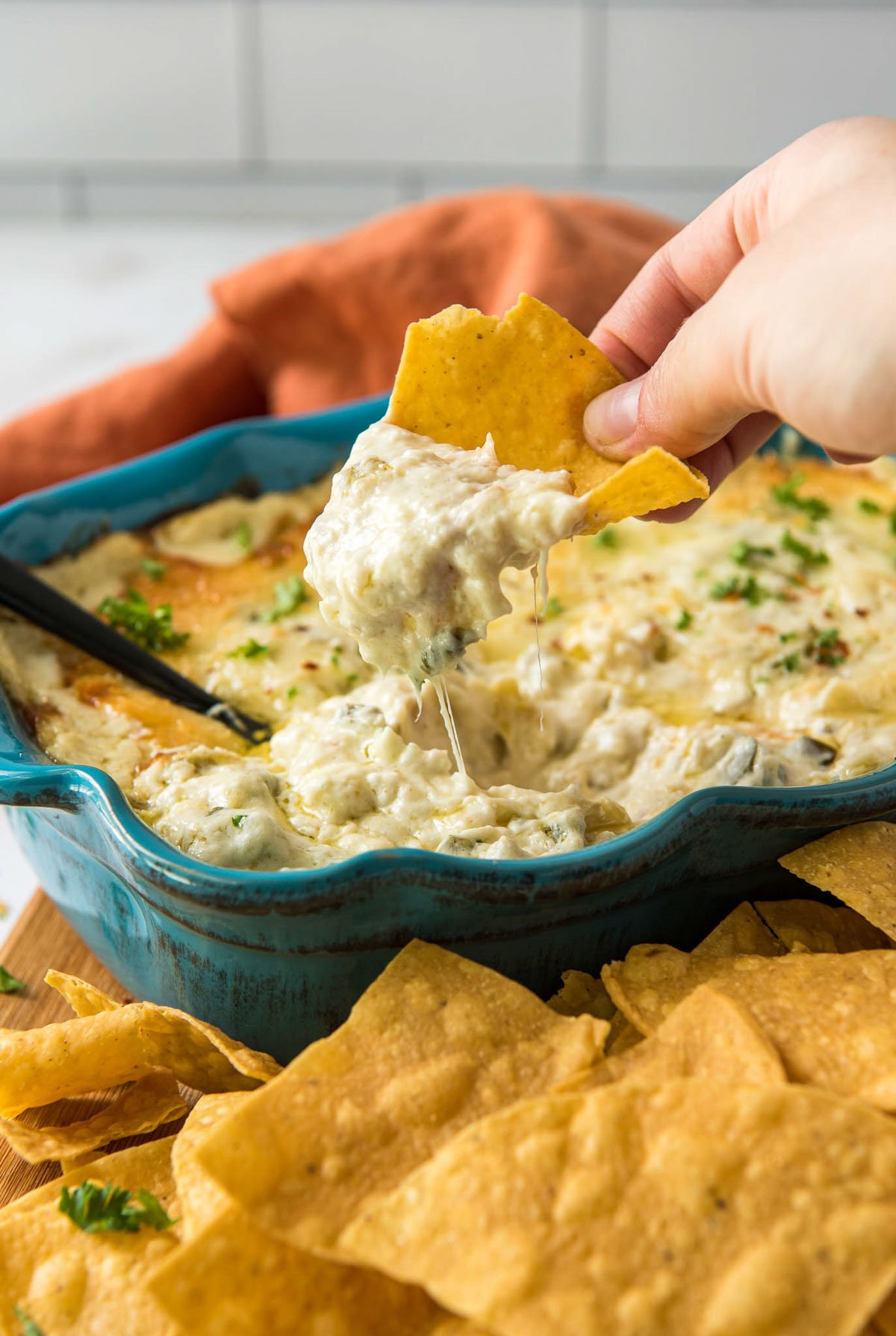 blue casserole dish, a hand, tortilla chips, orange napkin, hor artichoke dip, a spoon