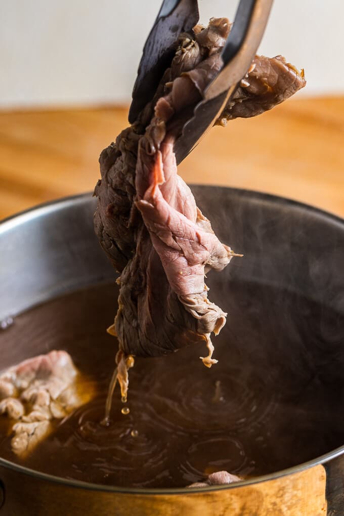 Dipping roast beef into pan of beef stock.