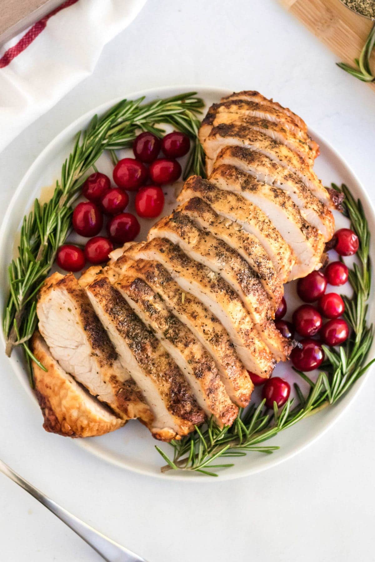 white platter, rosemary, cranberries, sliced turkey breast, fork