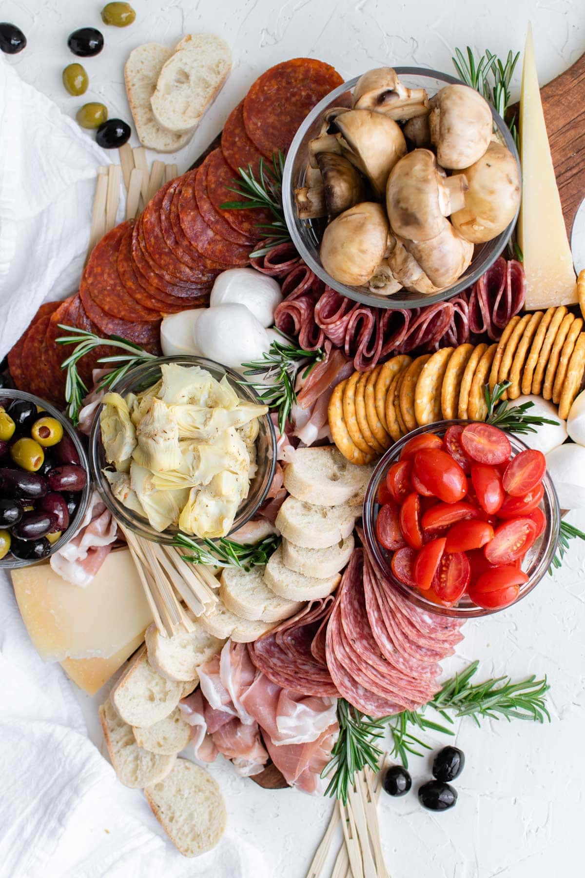 a wooden board, mushroom, salami, cheese, thyme, olives, tomatoes, crackers, bread, artichokes