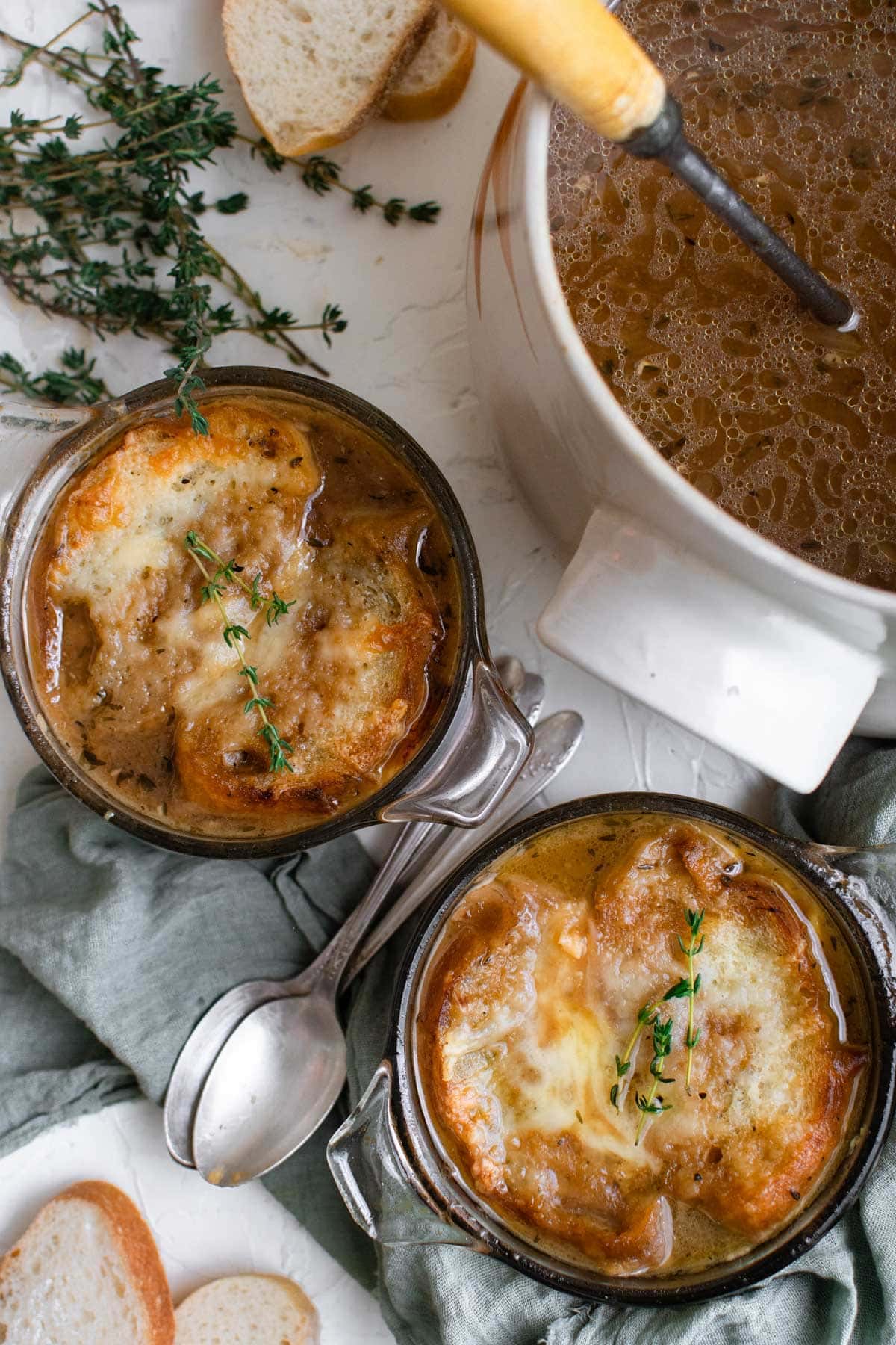 a pot of onion soup, bowls with cheesey toast on top, spoons, thyme leaves