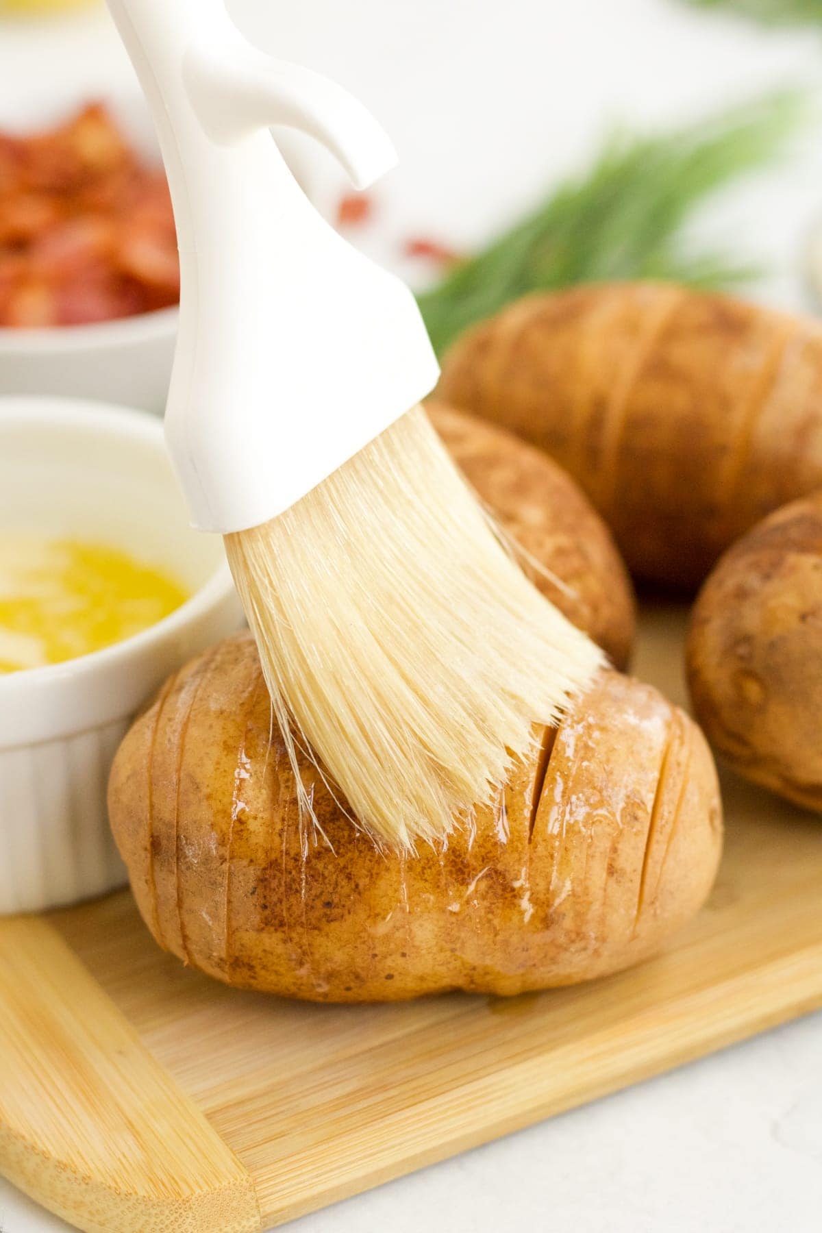 Olive oil being brushed on a russet potato to make Hasselback potatoes