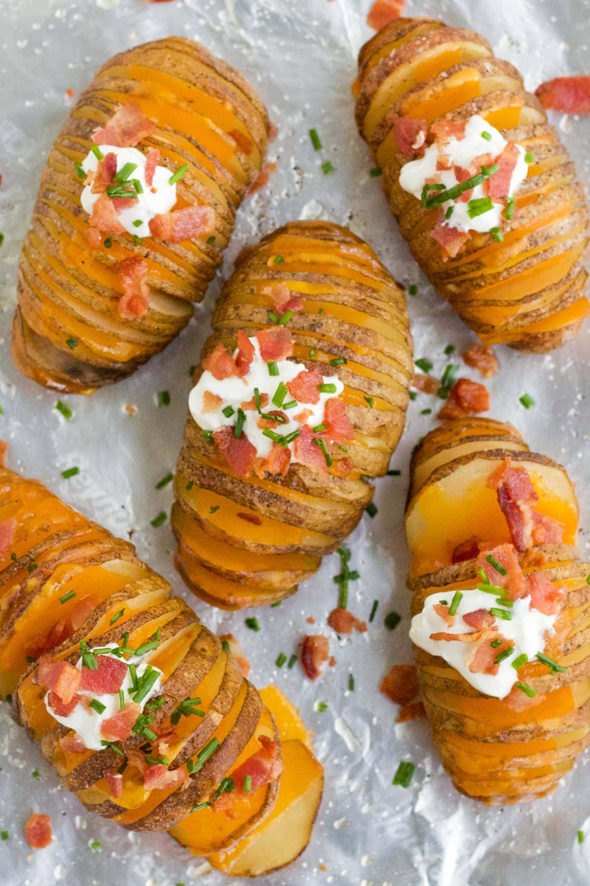 Hasselback Potatoes on a baking sheet with sour cream, bacon, cheddar cheese and chives. 