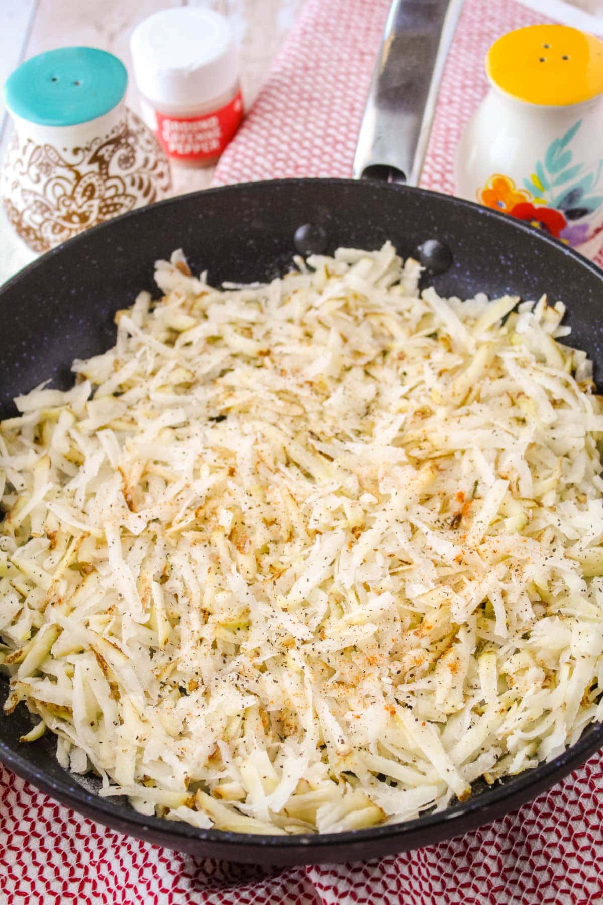 shredded potatoes in a skillet with salt, pepper, and cayenne