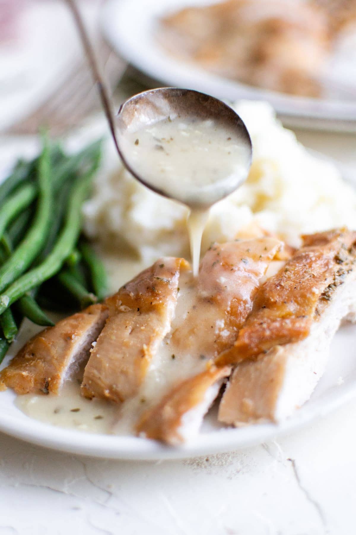 white plate, turkey sliced, green beans, mashed potatoes, spoon with gravy