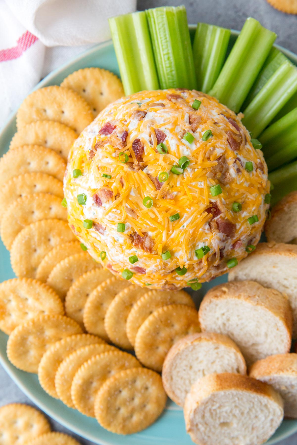 blue plate, crackers, slices of bread, celery, cheeseball with cheese, bacon and green onions