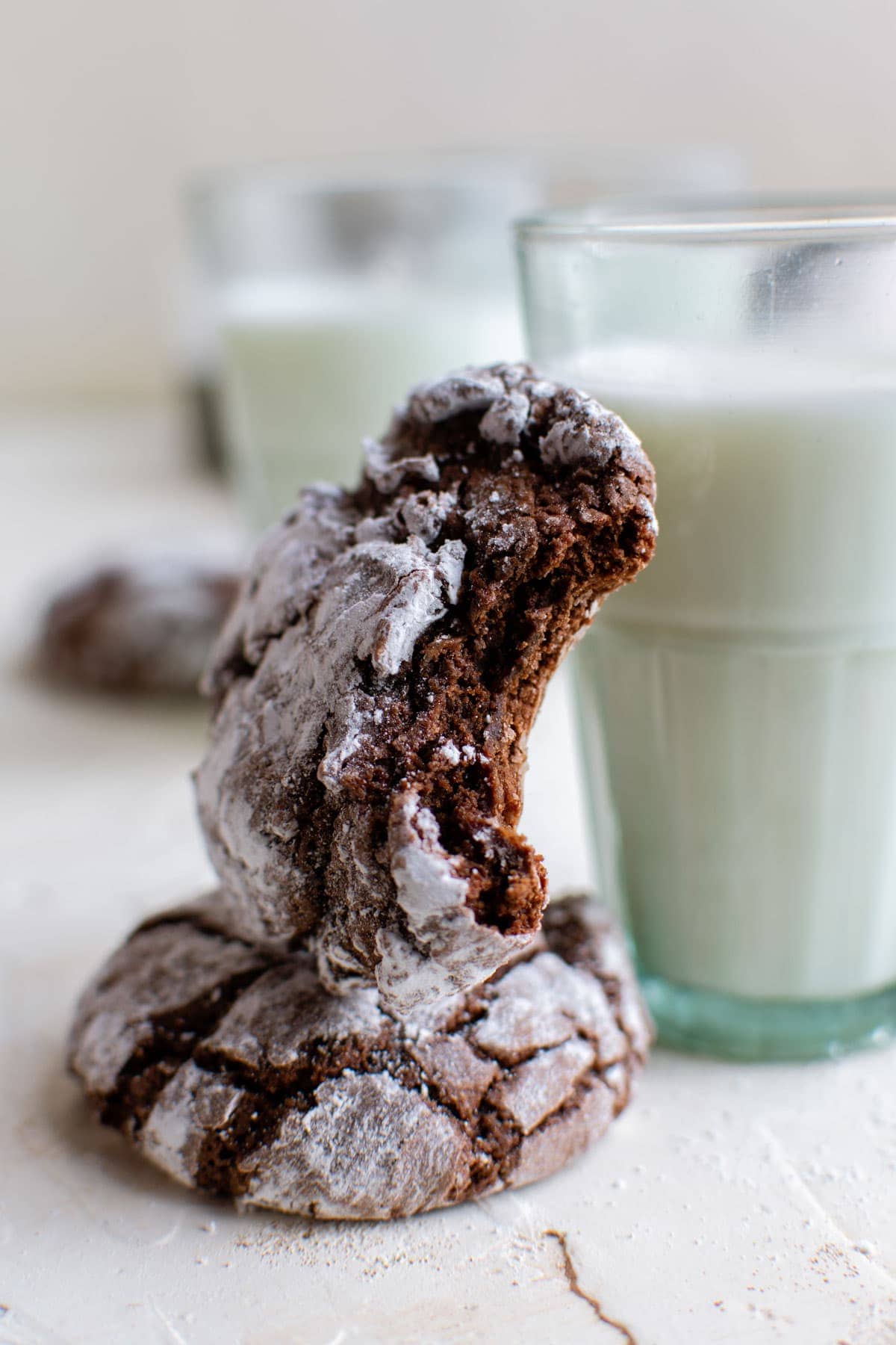 glass of milk, chocolate crinkle cookies, one with a bit in it.