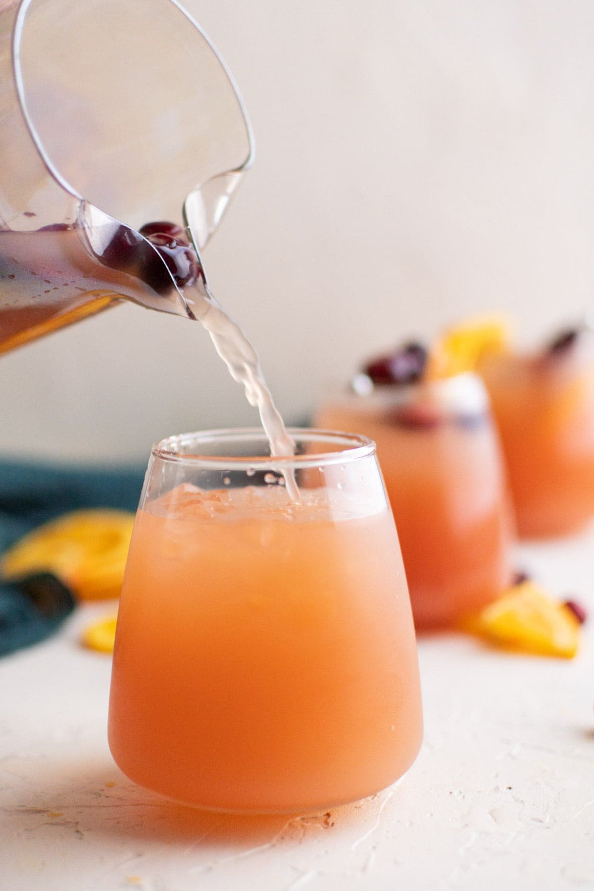 glasses of christmas punch, pitcher, stream of punch into glass, blue napkin, orange slices, cranberries