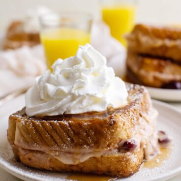 white plate, cranberry cream cheese french toast sandwich, orange juice, whipped ream