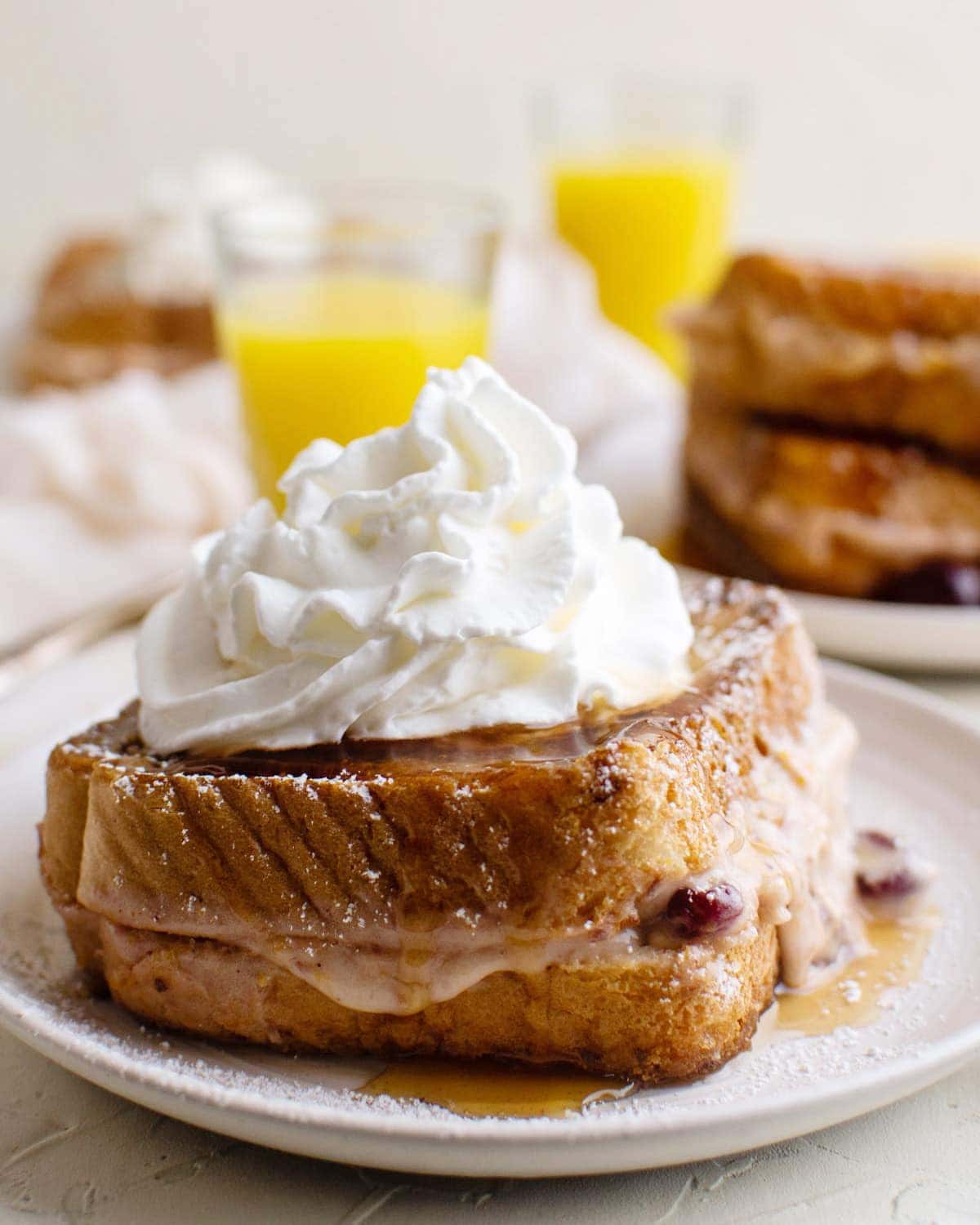 white plate, cranberry cream cheese french toast sandwich, orange juice, whipped ream